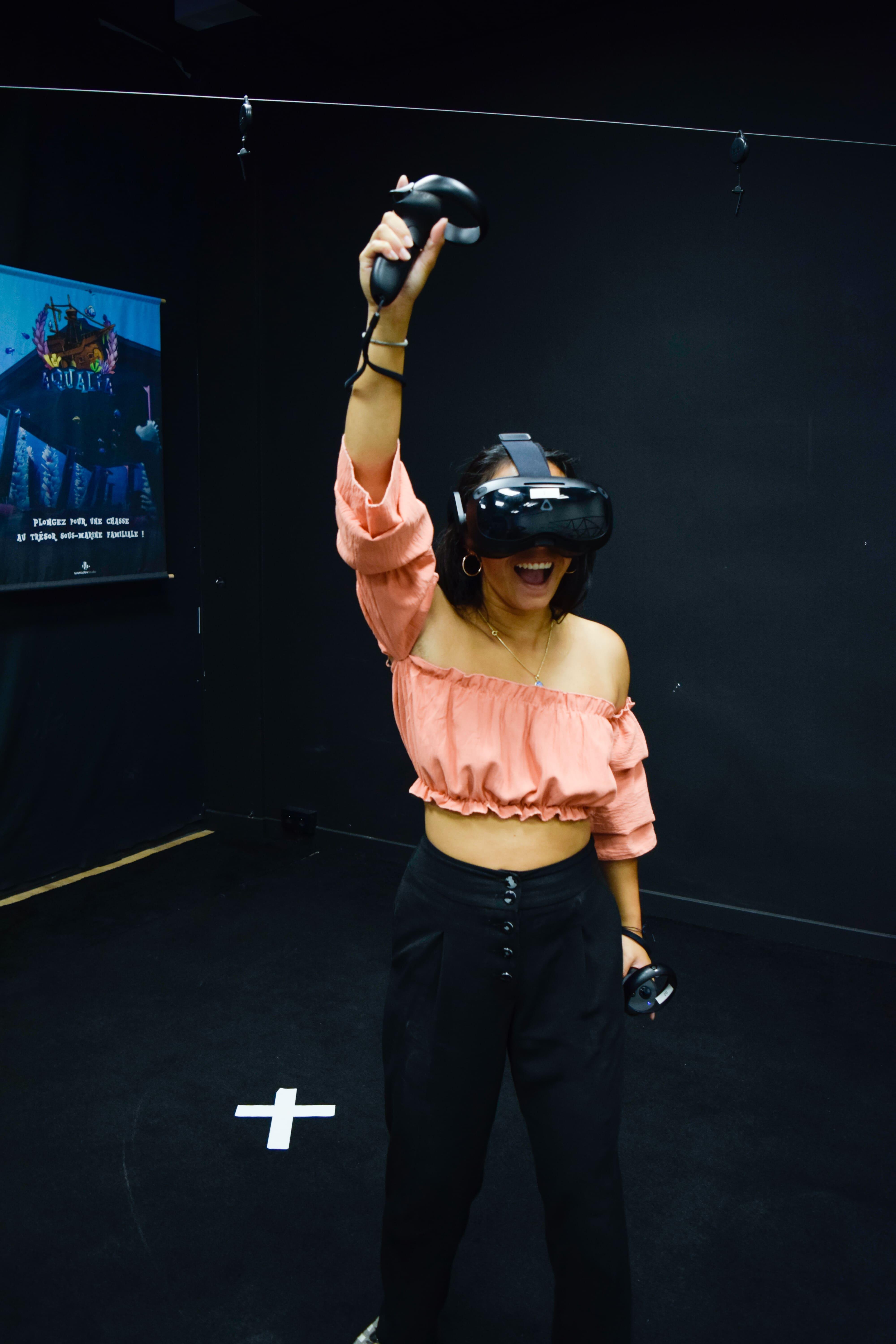 Une personne avec un casque et des manettes de réalité virtuelle qui sourie en levant le bras